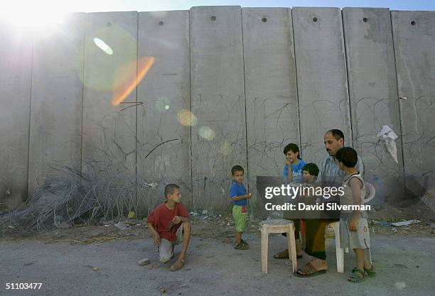 Palestinian man Nafiz Izzat reads to his family from an Islamic book where Israel's separation barrier runs alongside their house on July 21, 2004 as...