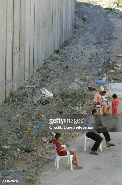 Palestinian man Nafiz Izzat sits with his family where Israel's separation barrier runs alongside their house July 21, 1004 in the West Bank village...