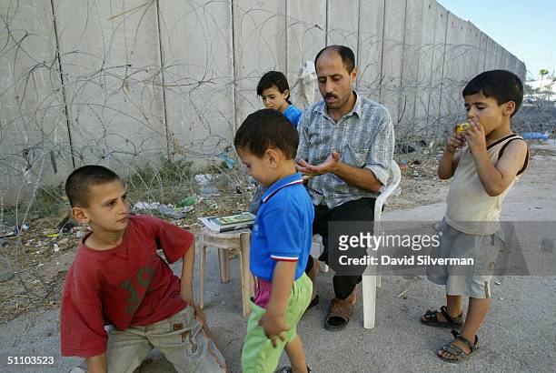 Palestinian man Nafiz Izzat sits with his children where Israel's separation barrier runs alongside their house July 21, 1004 in the West Bank...