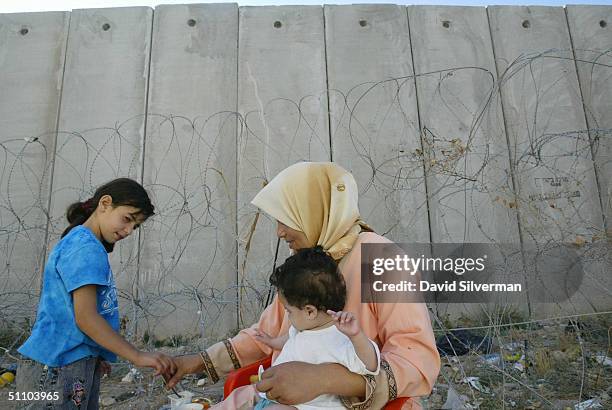 Palestinian mother Iman Izzat feeds two of her children, eight-month-old girl Muna and five-year-old girl Fatima, where Israel's separation barrier...