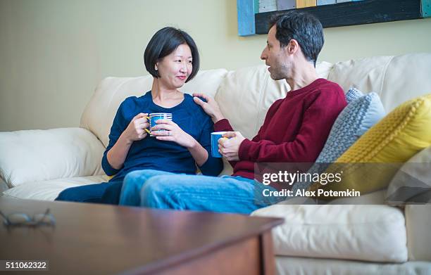 multi-ethnischen familie caucaian mann und koreanische frau, wie zu hause fühlen. - family on couch with mugs stock-fotos und bilder