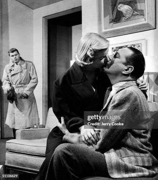 American actress Barbara Bel Geddes sits in the lap of Donald Cook as she kisses him, much to the concern of fellow actor Barry Nelson in a scene...