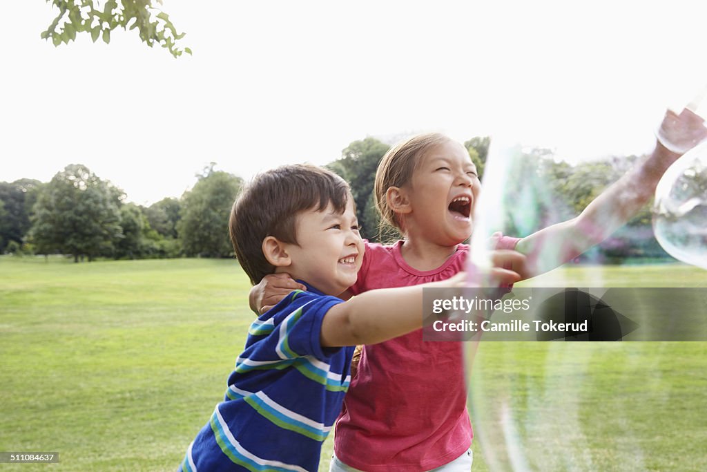 Brother and sister playing with bubbles in park