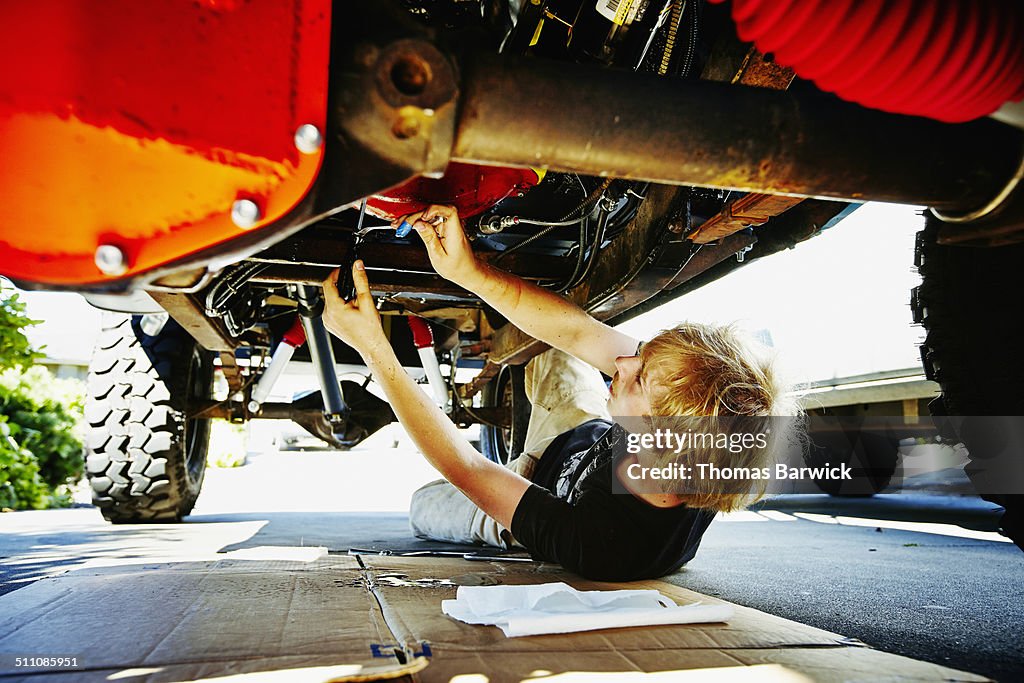 Teenager under vehicle replacing oil pan gasket