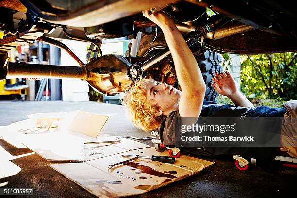 teenager lying on driveway replacing oil pan - car repair stockfoto's en -beelden