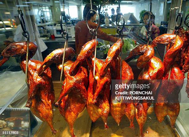 Thai food seller talks with a client next to roasted ducks on display at a restaurant in Bangkok, 27 July 2004. The latest Thai official figures show...