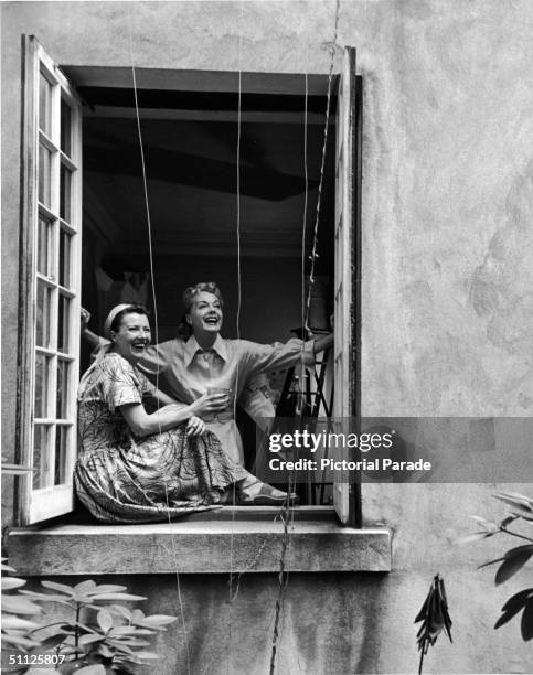 American actress, entertainer, and author Gypsy Rose Lee and her sister, actress June Havoc, laugh as they look out of a window, late 1960s.