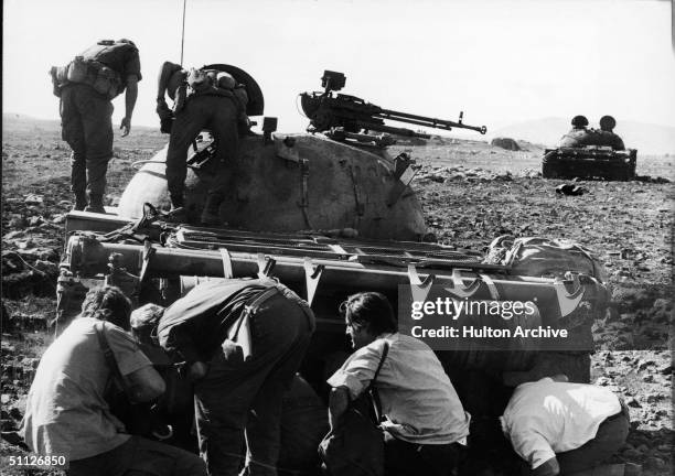 Photographers and radiomen find a wounded Syrian tank crewman hidden under his Soviet-built T-62 tank destroyed by Israelis during the Yom Kippur...