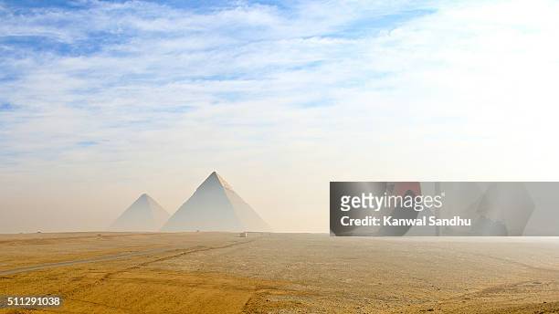 the giza pyramids viewed from distance in morning haze and blue skies - cléopâtre photos et images de collection