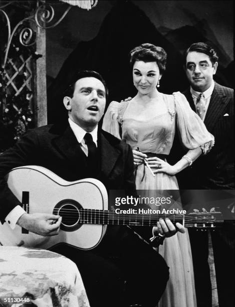 Austrian actor Theodore Bikel plays guitar and sings, watched by fellow actors Marion Marlowe and Kurt Kasznar in a scene of 'The Sound of Music' at...