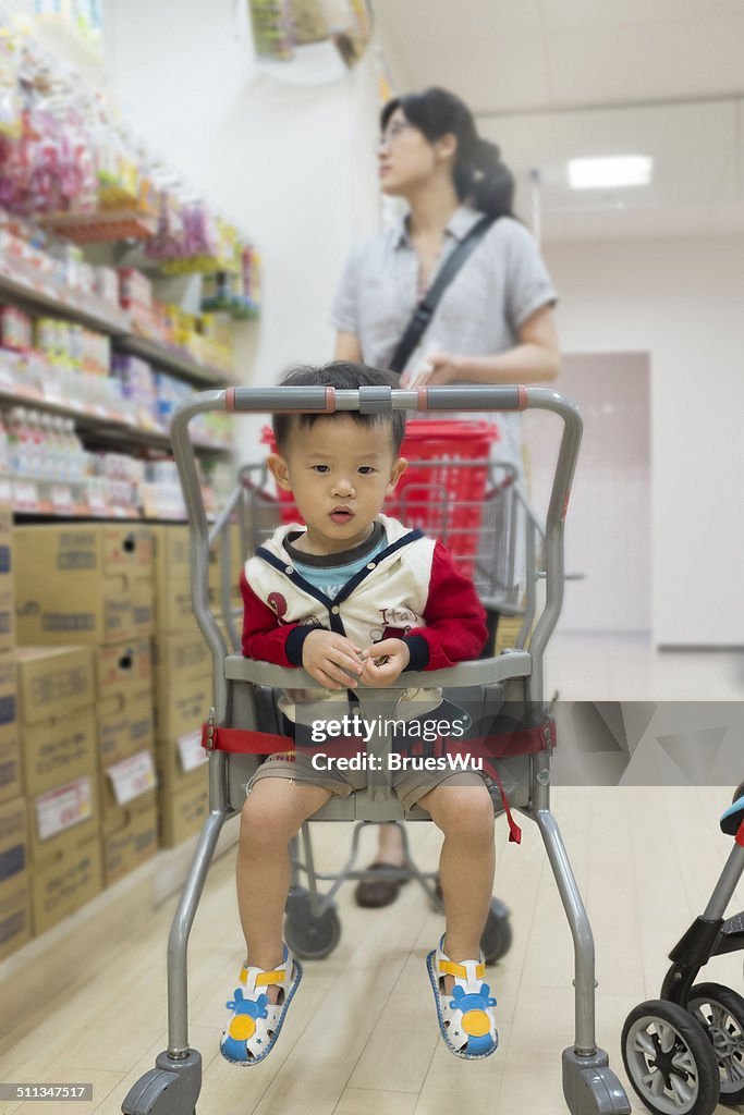 Baby boy sitting in shopping cart with mother