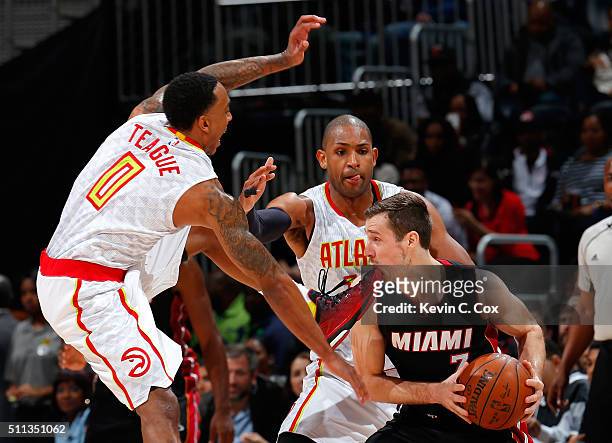 Goran Dragic of the Miami Heat takes a foot to the chin as he is defended by Jeff Teague and Al Horford of the Atlanta Hawks at Philips Arena on...