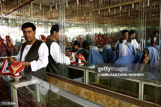 Burqa clad Afghan women are reflected in a mirror as they wait to peruse the wares of jeweller Abdul Qudus at his shop in Kabul, 02 August 2004. Some...