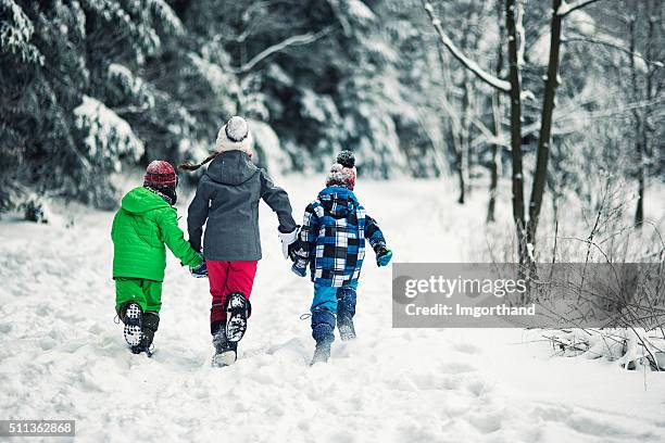 tre bambini correre nella foresta invernale - cappotto invernale foto e immagini stock