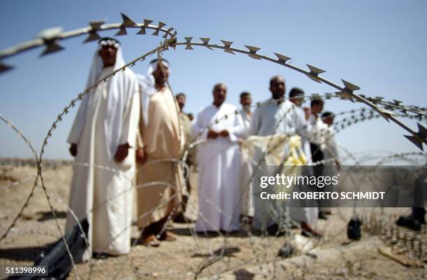 Iraqi men stand behind concertina wire as they wait outside the Abu Ghraib prison, 30 km west of Baghdad 08 May 2004. Hundreds of Iraqis gather in...