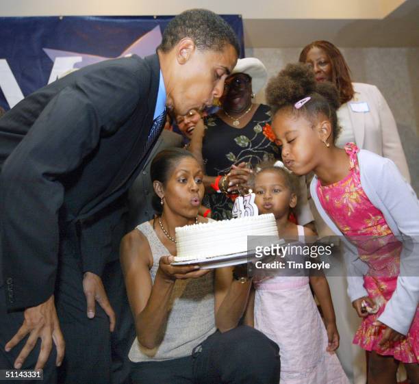 Barack Obama blows out candles on his birthday cake at his 43rd birthday celebration with his wife Michelle, who is holding the cake, and daughters...