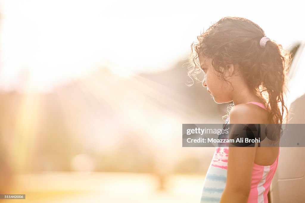 A thoughtful young girl standing in bright sunlight