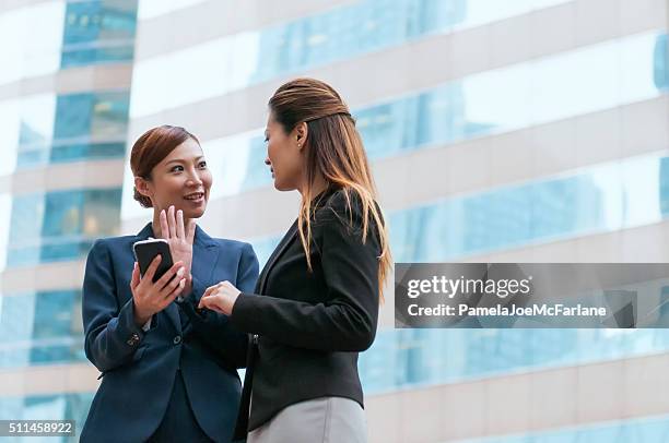 two asian businesswomen in discussion with smartphone outside office building - generic location stock pictures, royalty-free photos & images