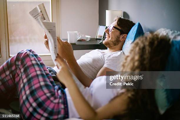 junges paar lesen zeitung im bett - junger mann liest zeitung stock-fotos und bilder