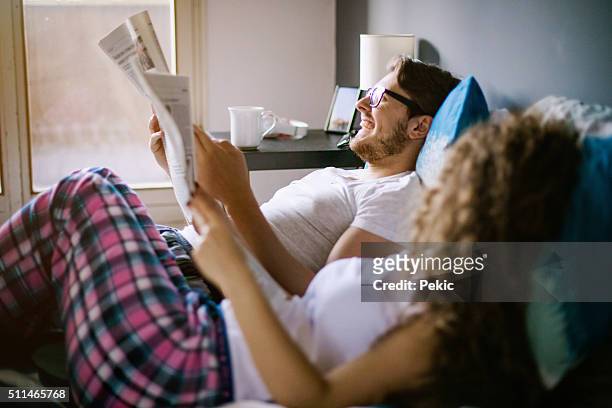 young couple reading newspaper in bed - read and newspaper and bed stock pictures, royalty-free photos & images