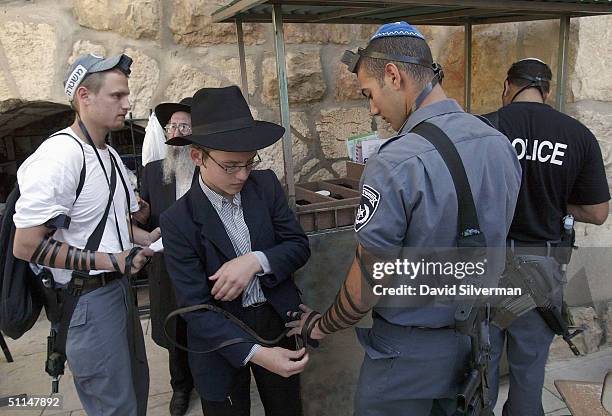 An ultra-Orthodox Jewish youth and his father help Israeli policemen wear Tefillin during their morning prayers at the Western Wall, Judaism's...