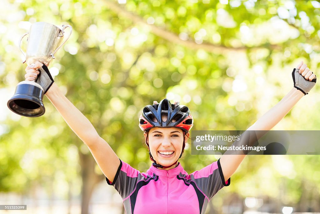 Alegre mulher ciclista usando capacete segurando o troféu