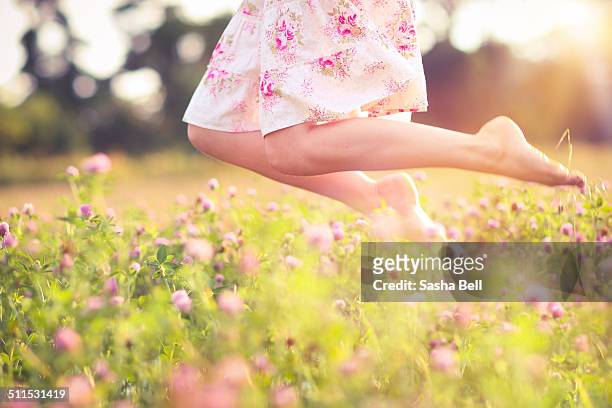 girl jumping in pink clover meadow field - frau wiese bewegt stock-fotos und bilder