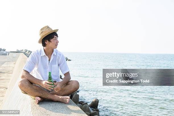 young man sitting on breakwater - groyne photos et images de collection