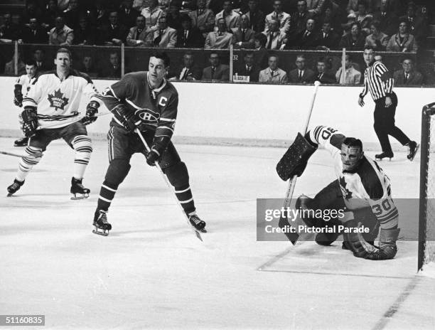 Goalie Terry Sawchuk of the Toronto Maple Leafs watches the puck while Jean Beliveau of the Montreal Canadiens waits in front of the net during Game...