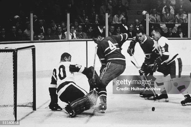 Goalie Terry Sawchuk of the Detroit Red Wings makes the save on the shot by Jean Beliveau of the Montreal Canadiens as Gordie Howe of the Red Wings...