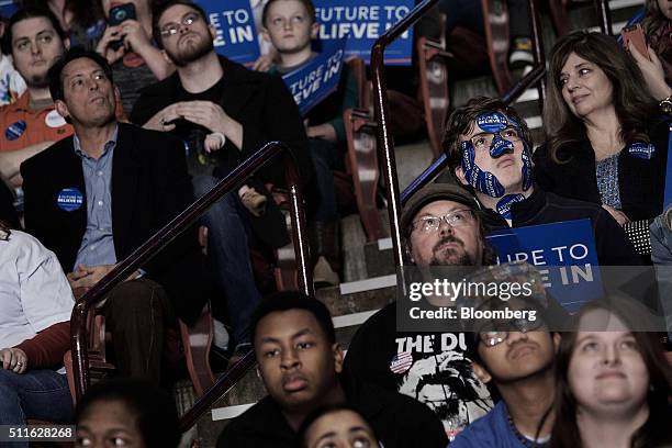 An attendee with stickers covering his face listens as Senator Bernie Sanders, an independent from Vermont and 2016 Democratic presidential...