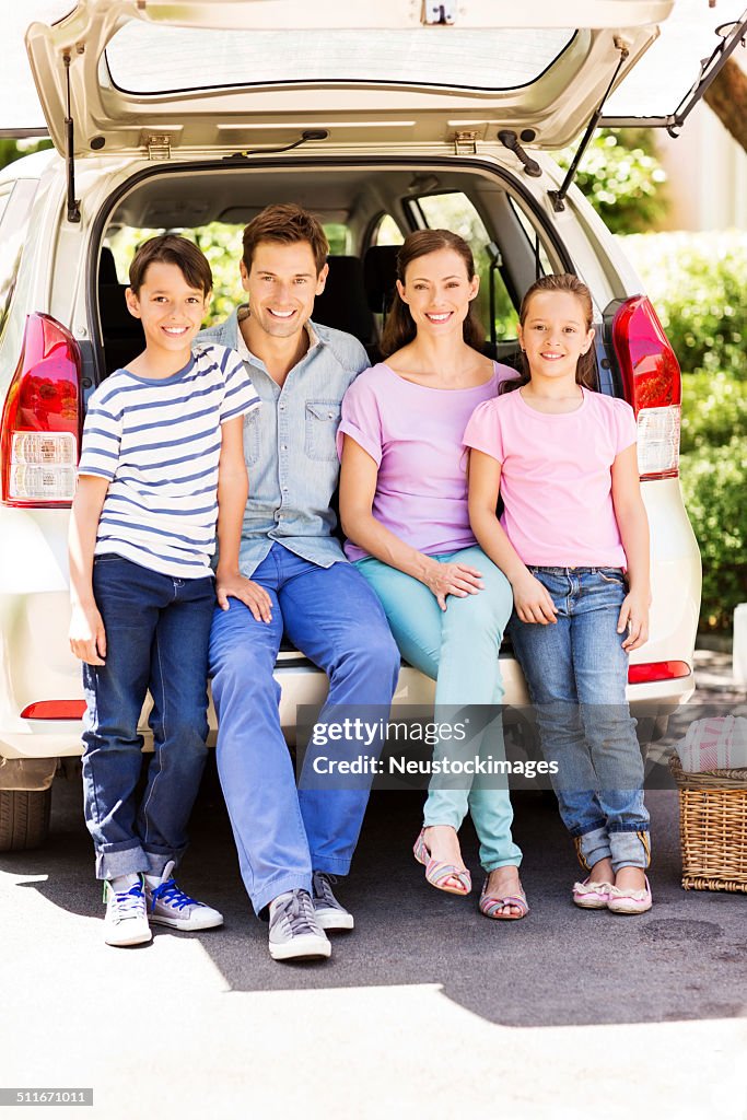 Smiling Family Sitting In Car Trunk On Street