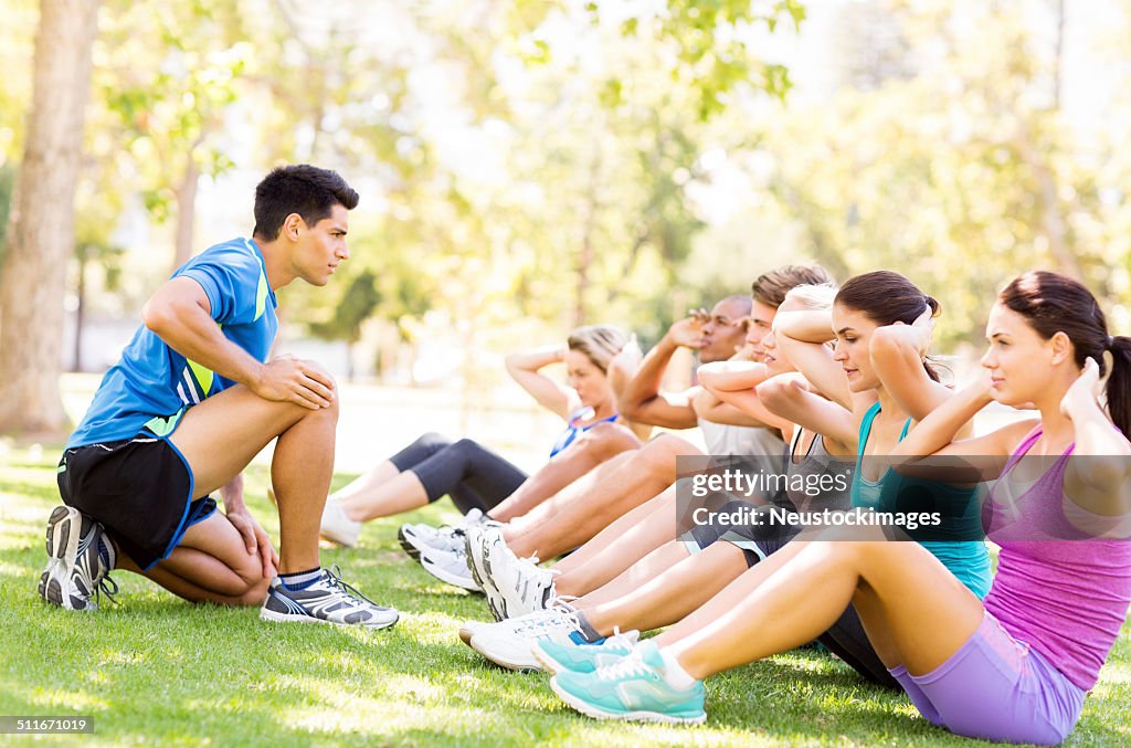 Fitness Instructor Motivating People In Doing Sit-Ups At Park
