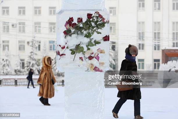 Local residents dressed in fur pass an ice sculpture containing roses and rose petals on Lenin Square in Yakutsk, Sakha Republic, Russia, on Sunday,...