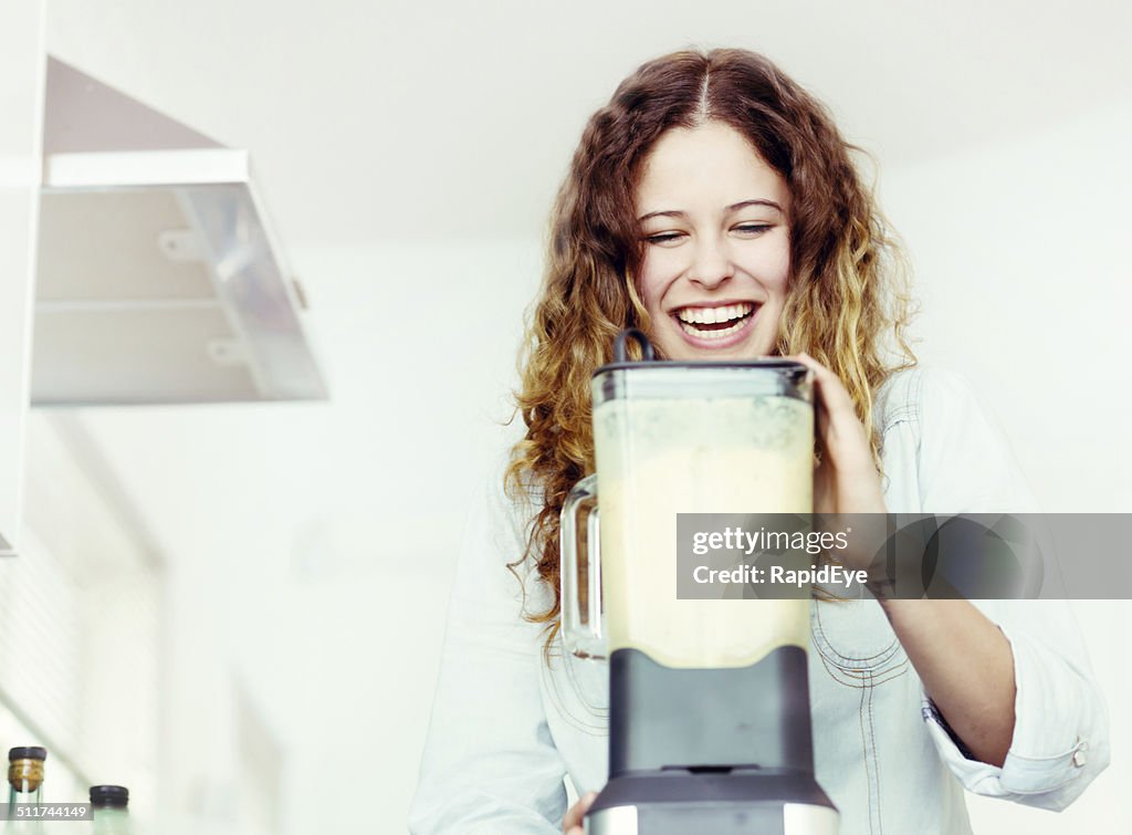 Smiling young woman busy in kitchen with blender, making smoothie