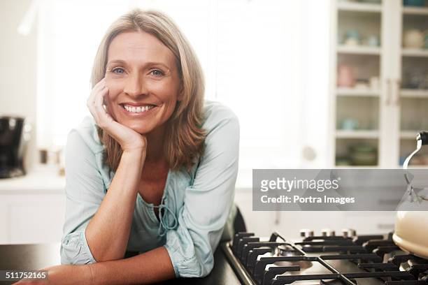 happy woman leaning on kitchen counter - female blonde blue eyes stock-fotos und bilder