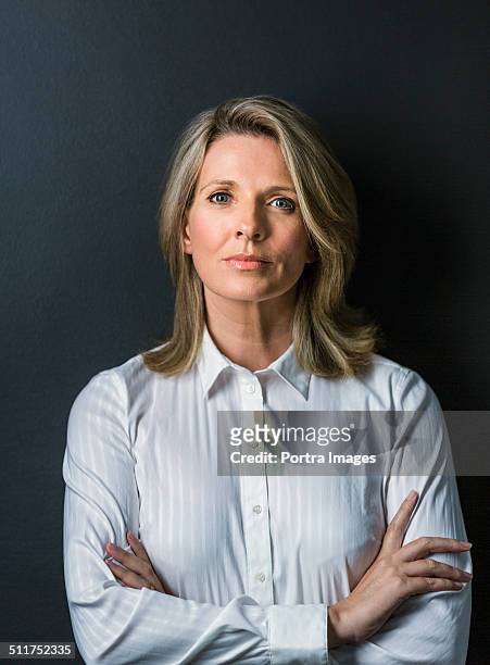 mature businesswoman standing arms crossed - blonde blue eyes stock-fotos und bilder