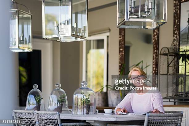 senior woman with newspaper at table - sitting at table looking at camera stock-fotos und bilder