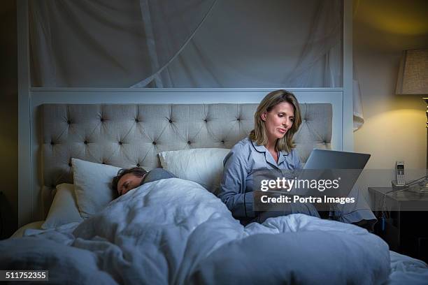 woman using laptop while man sleeping on bed - woman 45 sleeping stock pictures, royalty-free photos & images