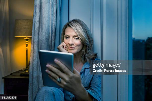 mature woman using digital tablet at home - woman ipad stockfoto's en -beelden
