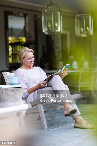 senior woman reading magazine at porch - frau zeitschrift liest stock-fotos und bilder