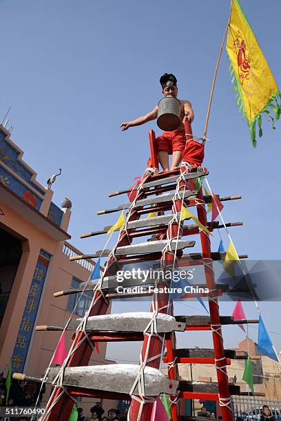 Barefoot stuntman carrying a pail of water with his mouth, climbs a ladder with blades for rungs during an annual show of daredevil skills in Taixi...