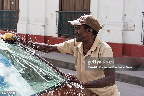 Senior Afro Caribbean man washing a tourist car outside the Santa Rosalia Restaurant. While tourist have lunch this man washes their autos for a tip...