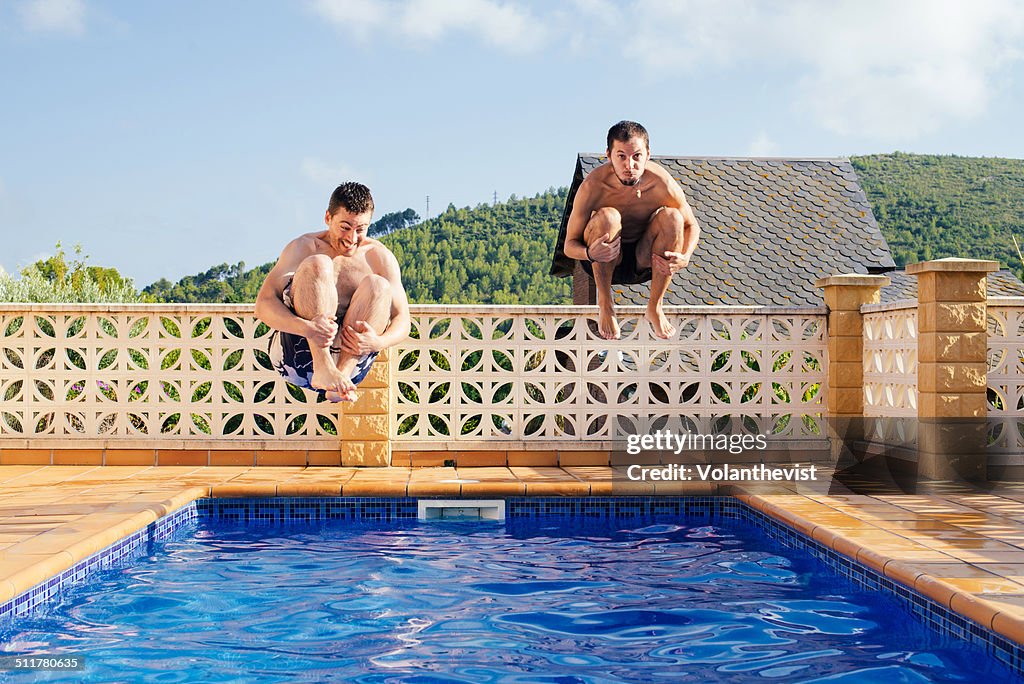 Two young men jumping into swimming pool