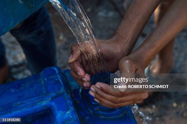 Resident of the eastern New Delhi neighborhood of Sanjay Camp cups his hands around the spout of a jerry can as another man pours in water at a water...