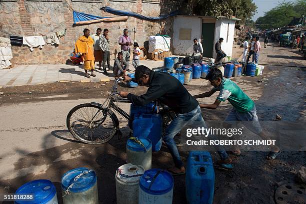 Two residents of the eastern New Delhi neighborhood of Sanjay Camp push a bicycle loaded with water containers as they head home from this water...