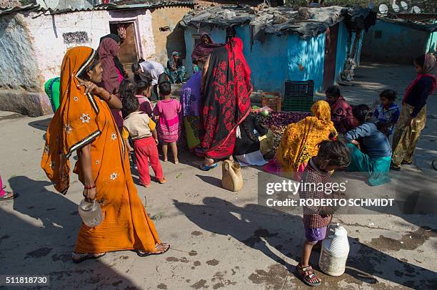 An Indian girl looks at her hands while taking a break from hauling a jerry can filled with water to her home from a distribution point in the...