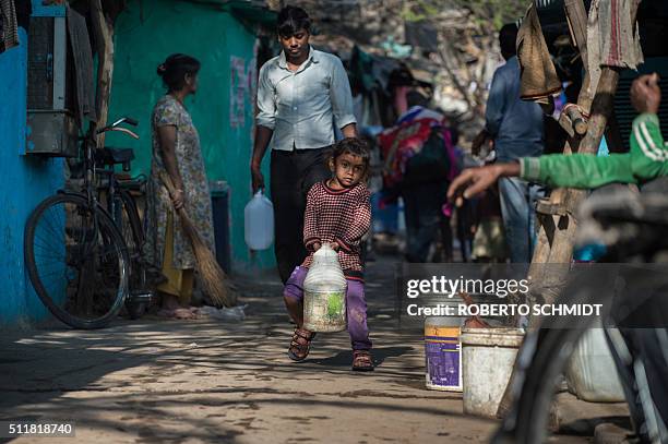 An Indian girl struggles to carry a jerry can filled with water as she helps family members fetch water from a distribution point in the low-income...