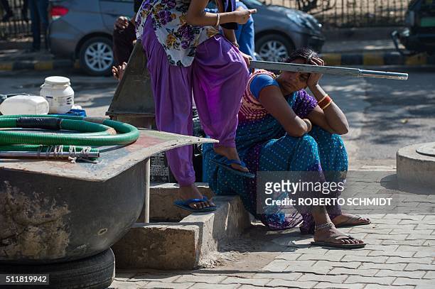 Indian residents sit on a dry water pump as they wait for fresh water supplies to arrive by truck at a water distribution point in the low-income...
