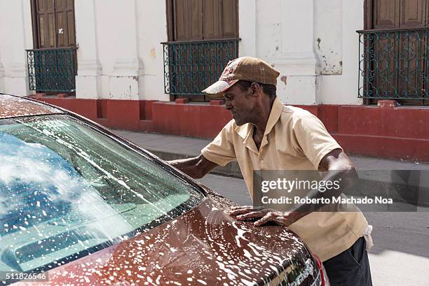 Senior Afro Caribbean man washing a tourist's car outside the Santa Rosalia Restaurant. While tourist have lunch this man washes their autos for a...